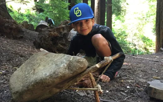 a boy with a blue hat and blue shirt sitting on a log