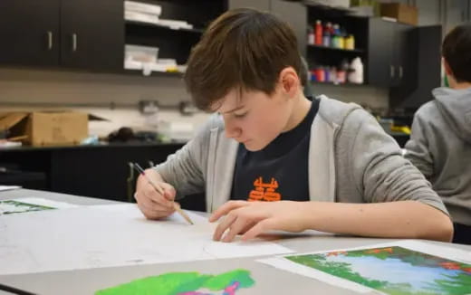 a boy sitting at a table writing on a paper