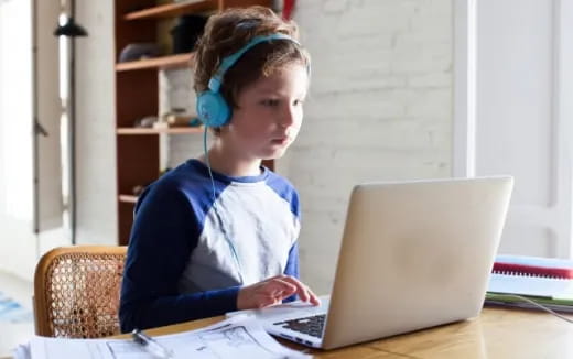 a boy wearing headphones and sitting at a table with a laptop