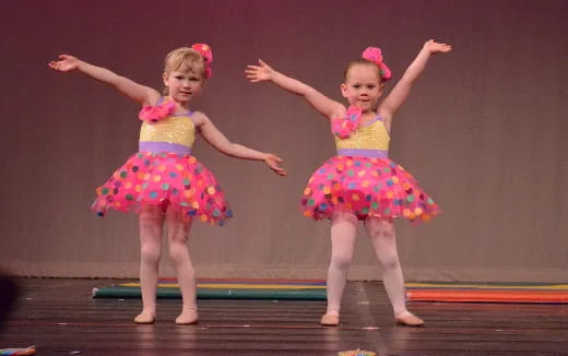 two girls wearing dresses and dancing on a stage