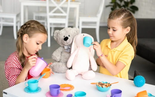 two girls sitting at a table with a stuffed animal