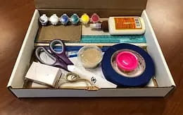 a box with a pair of scissors and a box of paints