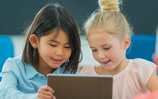 a couple of young girls looking at a tablet