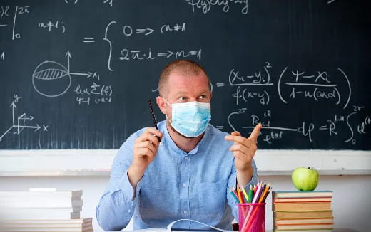 a man wearing a mask and holding a pen in front of a blackboard