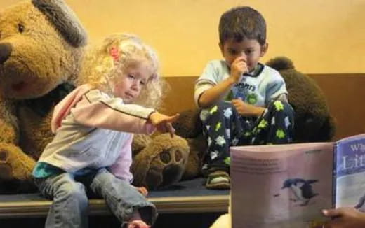 a couple of kids sit on a couch with teddy bears