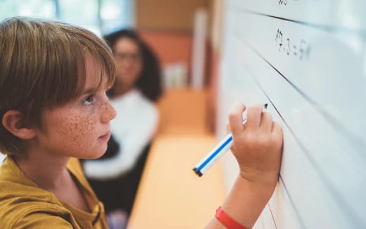 a young boy writing on a whiteboard