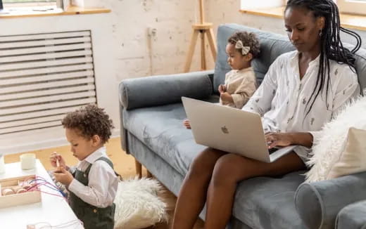 a woman and a couple of children sitting on a couch looking at a laptop