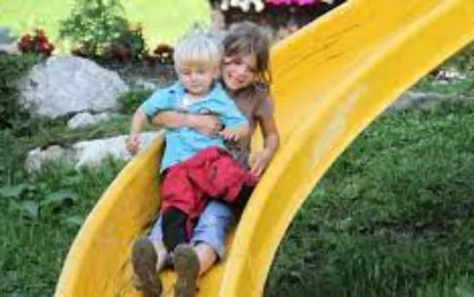 a couple of children in a yellow slide in a grassy area