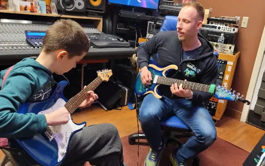a person playing a guitar next to a boy sitting on a chair