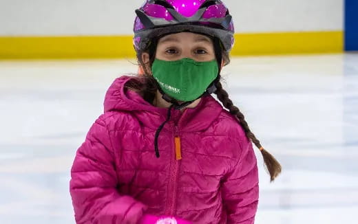 a girl wearing a pink jacket and helmet on ice