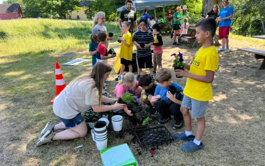 a group of children gathered around a woman and a man planting a tree