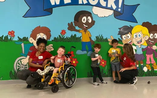 a group of kids and a person in a wheelchair in front of a wall with cartoon characters