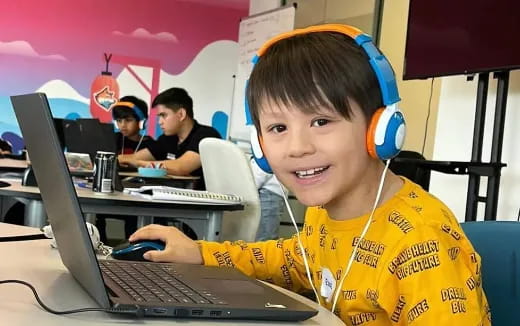 a boy wearing headphones and sitting at a desk with a laptop