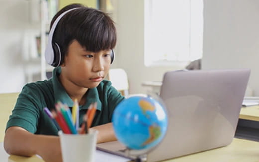 a boy wearing headphones and sitting at a desk with a computer