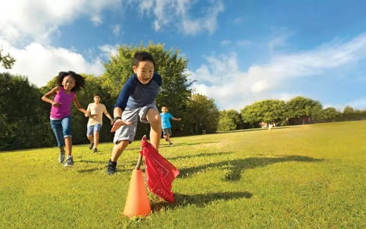 a group of kids running around a cone on a grass field