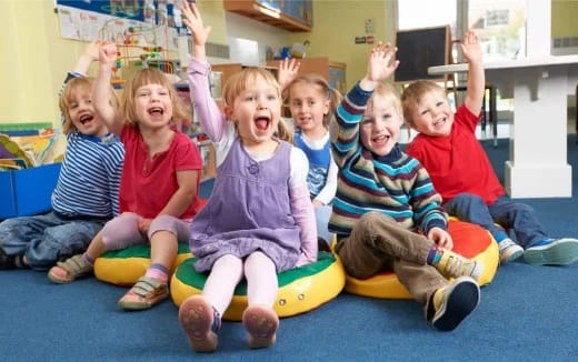 a group of children sitting on a mat with their arms raised