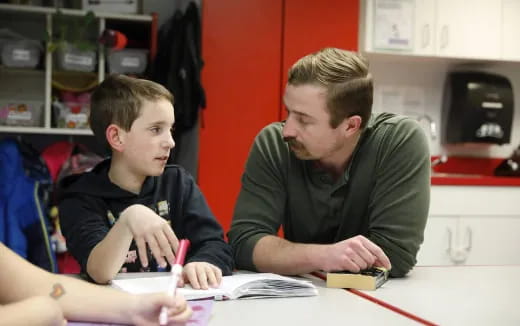 a couple of boys sitting at a table looking at papers