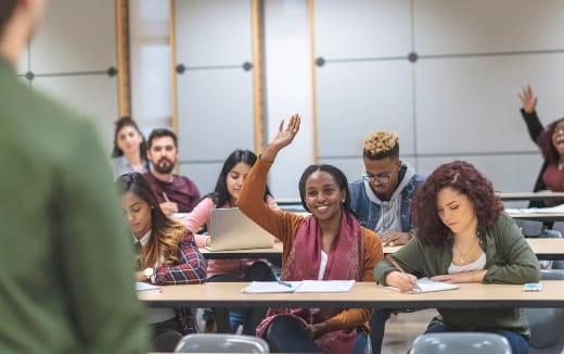 a group of people sitting at desks with their hands up