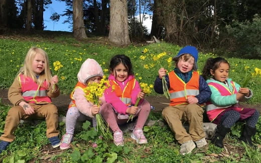 a group of children sitting in a grassy area with flowers