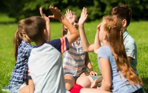 a group of children sitting on the grass with their hands up