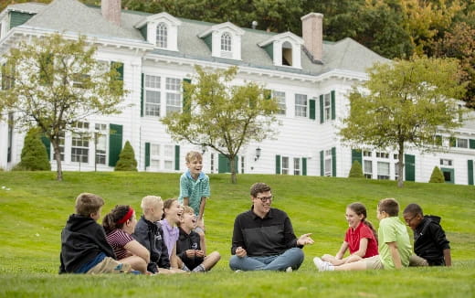 a group of people sitting on the grass in front of a white house