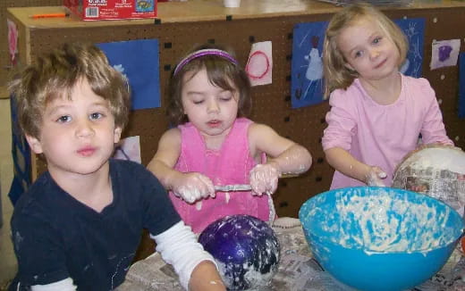 a group of children sitting in a room with a bowl of food