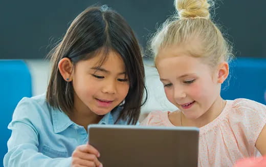 a couple of young girls looking at a laptop