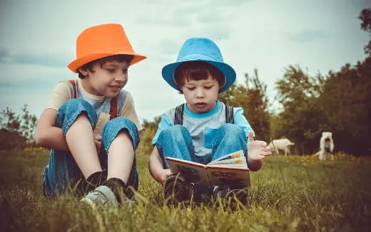 a couple of kids wearing hats and looking at a book