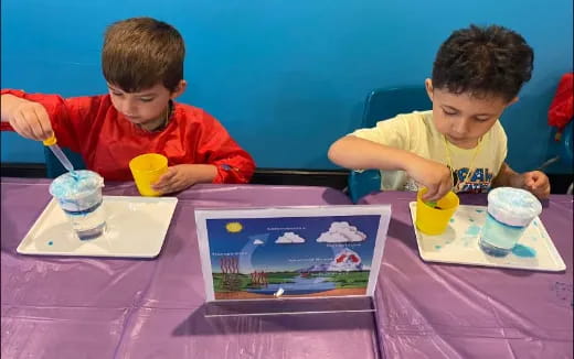 a couple of boys sitting at a table with food and drinks