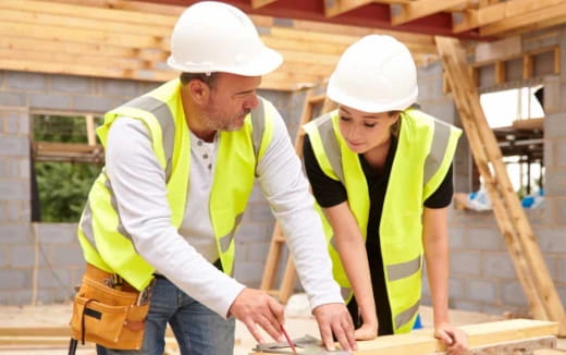 a man and a woman wearing hard hats and working on a piece of wood