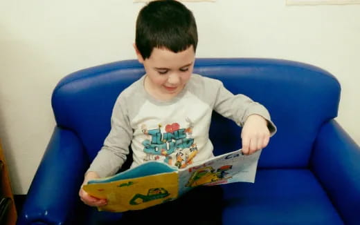 a child sitting on a blue chair reading a book