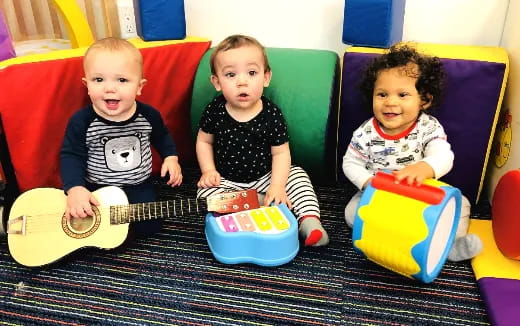 a group of babies sitting on a couch playing instruments