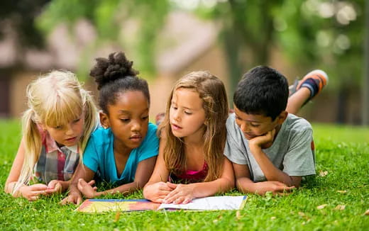 a group of children sitting on the grass writing on paper