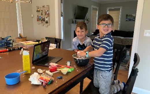 a couple of boys sitting at a table with a laptop and food
