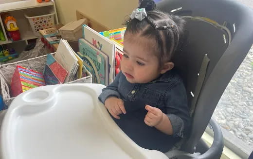 a baby sitting in a highchair with a book and a basket of books