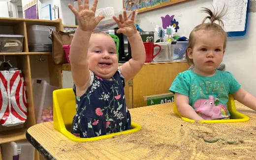 a couple of young girls sitting at a table with their hands up