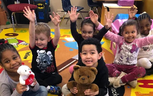 a group of children sitting on the floor with their hands up