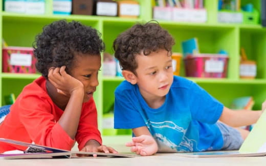 a couple of children sitting at a table looking at a book