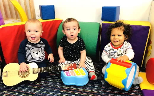 a group of babies sitting on a couch playing a guitar