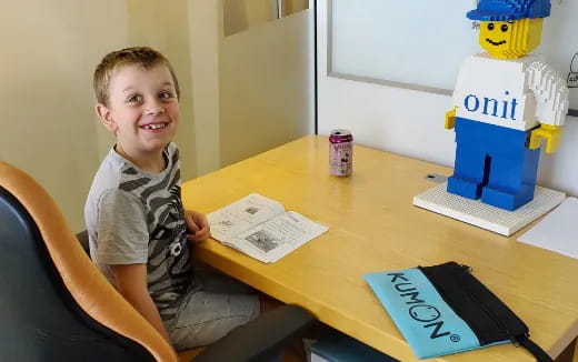 a boy sitting at a table with a paper and a toy