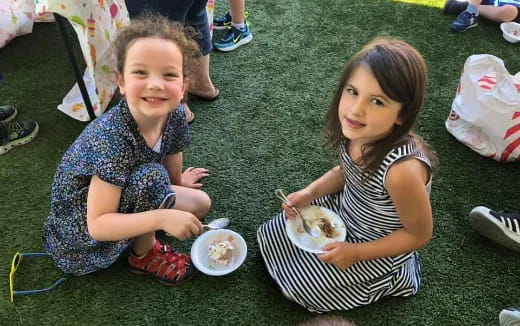 a couple of girls sitting on the grass eating food