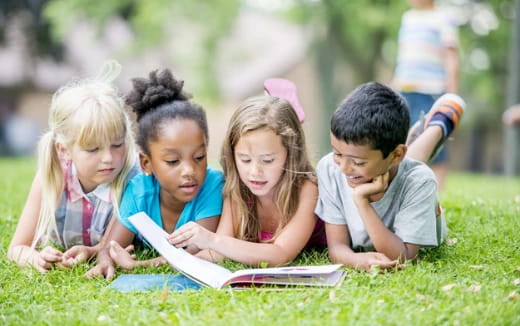 a group of children sitting on the grass looking at a book