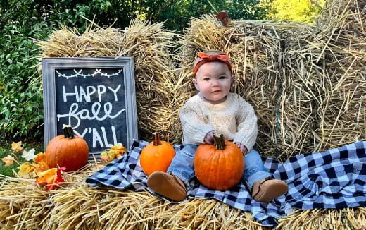 a baby sitting on a blanket with pumpkins and a sign