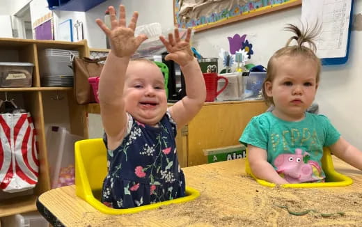 a couple of children sitting at a table with their hands up