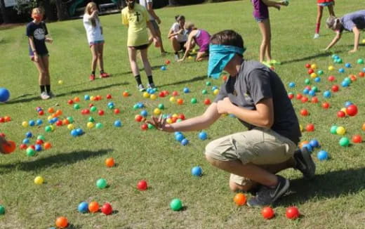 a person kneeling in the grass with balls on the ground