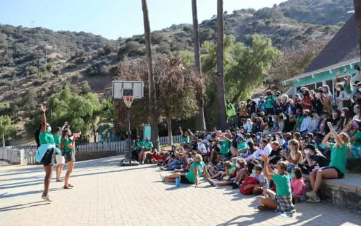 a group of people sitting on the ground in front of a basketball hoop