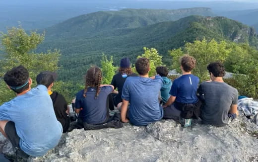 a group of people sitting on a rock overlooking a forest