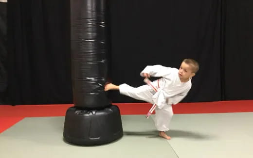 a baby in a karate uniform kicking a black object