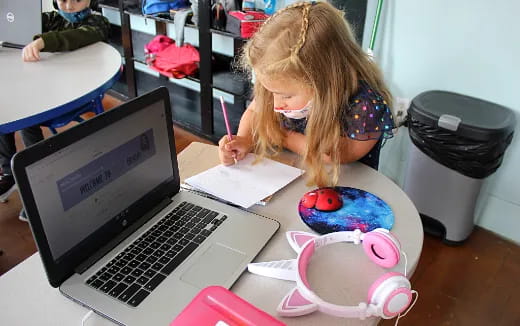 a girl sitting at a desk with a laptop and a pen