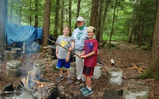 a group of boys standing in the woods with a fire and a tent